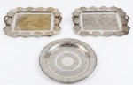 Três bandejas em metal espessurado a prata com fundo cinzelado e bordas vazadas da marca Regia. Med.: bandejas retangulares: 37,5cm de largura x 30cm de altura, bandeja redonda: 2,5 de altura x 34cm de diâmetro.