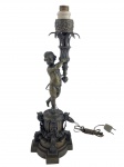 Escultura em bronze representando querubim segurando tocha sobre coluna  romana com cabochons e guirlanda floral. 43 cm.
