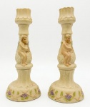 Par de castiçais em buiscuit, possivelmente, alemão com base vegetalista e corpo com figuras angelicais em relevo. 18cm.