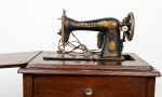 Máquina de Costura Singer. Máquina de costura doméstica antiga da tradicional manufatura Singer, em ferro fundido esmaltado na cor preta, com decoração floral em policromia e filetes dourados ( com falhas). Montada em gabinete de madeira nobre com acabamento em tom de mogno. Motor funcionando e pedal de alumínio.