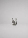 Escultura decorativa em vidro artístico incolor, maciço e modelado a quente, representando esquilo sentado, com patas dianteiras elevadas, cabeça voltada lateralmente e cauda volumosa arqueada sobre o dorso. Apresenta formas estilizadas e detalhes anatômicos moldados no próprio vidro. Medindo: