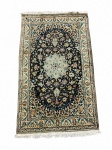 NAIN - Tapete persa de manufatura em lã sobre algodão, apresentando campo azul-marinho com medalhão floral polilobado em azul-claro, marfim, bege e vinho, envolvido por palmetas, flores e ramagens simétricas. Barra principal marfim com composição floral contínua entre faixas secundárias. Medindo: 2,10 X 1,27