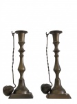 Par de castiçais confeccionados em metal com acabamento patinado, de fabricação indiana, conforme etiqueta original "Made in India". As peças apresentam base quadrada, haste torneada e porta-vela com prato coletor de cera, acompanhados de apagadores de velas (snuffers) articulados, acessório tradicional utilizado para extinguir a chama sem dispersar fumaça ou respingos de cera. Medindo 23 x 8