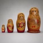 Matriosca soviética composta por quatro bonecas encaixáveis em madeira torneada, decoradas manualmente com figuras femininas, lenços, aventais e motivos florais policromados. A maior peça mede 12 cm de altura x 6,5 cm de diâmetro, enquanto a menor mede 4 cm de altura x 2 cm de diâmetro. A composição apresenta traços lineares em preto e detalhes em vermelho, rosa e verde, distribuídos de forma individualizada entre as figuras. A maior boneca preserva etiqueta original em cirílico da Fábrica de Souvenires de Sharanga, vinculada à produção de artesanato artístico da região soviética de Gorky. A gradação das dimensões, a pintura popular russa e a identificação de fábrica conferem ao conjunto interesse histórico e colecionável.