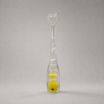 Vaso escultórico da manufatura sueca Vas Vitreum, produzido em cristal incolor de corpo espesso e elevada verticalidade. Apresenta base com inclusão interna em amarelo intenso, envolvida pelo cristal transparente, seguida por elementos suspensos e longo colo orgânico, finalizado por boca assimétrica e ondulada.A configuração integra a série Gloria, associada ao designer e mestre vidreiro sueco Mikael Kenlind, representante da quinta geração de artesãos da Vas Vitreum. A peça conserva a etiqueta original da manufatura, fundada em Vadstena, Suécia, e reconhecida pela produção manual de cristal artístico.