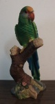Esplendida escultura de papagaio em resina, repousando sobre tronco de arvore, com rica policromia e uma flor na base do tronco. Med. 21 cm altura.