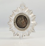 RELICÁRIO DE SANTA MARIA MADALENA  RELICARIO SEISCENTISTA  COM TECA EM CRISTAL DE ROCHA ESCULPIDO E MOLDURA EM PRATA DE LEI CONTENDO EM SEU INTERIOR FRAGMENTO DA PLACA EM MADEIRA ENVOLTA EM CERA QUE IDENTIFICAVA OS RESTOS MOTAIS DA SANTA QUANDO FORAM DESCOBERTOS. NA PARTE FRONTAL UMA IMAGEM DA SANTA APRESENTADA COM LONGOS CABELOS, EM ATITUDE DE ORAÇÃO TENDO A SUA FRENTE UM CRÂNIO E UM FRASCO DE PERFUME (SEUS ATRIBUTOS). A PLACA É GUARNECIDA POR UM BORDADOEM FIO AZUL E BRANCO. RELICARIOS COM RELIQUIAS DE SANTA MARIA MADALENA SÃO EXTREMAMENTE RAROS PELA ESCASSEZ DE SUAS RELIQUIAS. ESTE EM PARTICULAR FOI CONCEBIDO COMO UMA JÓIA  COM A TECA PRIMOROSAMENTE ESCULPIDA EM CRISTAL COM FEITIO DE RESPLENDOR. EUROPA, SEC. XVII. 5 CM DE ALTURANOTA: A descoberta mais famosa das relíquias de Santa Maria Madalena ocorreu em dezembro de 1279, na cidade de Saint-Maximin-la-Sainte-Baume, na região da Provença, sul da França. Carlos II de Nápoles (Conde da Provença e sobrinho do rei São Luís) liderou escavações na cripta da antiga igreja de Saint-Maximin. Ele encontrou um antigo sarcófago de mármore datado do século IV. Segundo registros da época, ao abri-lo, exalava um perfume forte e doce, e havia uma tábua de madeira com a inscrição em latim: "Hic requiescit corpus beatae Mariae Magdalenae" (Aqui repousa o corpo da bem-aventurada Maria Madalena).  Um papiro datado de 710 d.C. também foi encontrado no local, atestando que os restos mortais haviam sido escondidos séculos antes para protegê-los de invasões sarracenas. As relíquias da santa foram divididas e abrigadas em diferentes locais de devoção: Saint-Maximin-la-Sainte-Baume: A principal delas é um crânio humano enegrecido, guardado em um relicário de ouro na Basílica de Santa Maria Madalena. San Giovanni dei Fiorentini: Na Itália, há uma capela onde está localizado o osso do pé esquerdo da santa, que a tradição aponta ter sido o primeiro a entrar no túmulo vazio após a Ressurreição. Outros locais: Fragmentos menores de ossos e relíquias de contato estão espalhados pelo mundo, como o mosteiro de Simonopetra (Grécia) e o Metropolitan Museum of Art (Nova York)