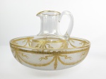 BACCARAT  SERVIU AO IMPERADOR DOM PEDRO II QUANDO HOSPEDADO NA FAZENDA SANTA MÔNICA EM 14 DE FEVEREIRO DE 1881. OPULENTO GOMIL E BACIA EM CRISTAL DE BACCARAT SUNTUOSAMENTE DECORADO EM OURO COM GUIRLANDAS E FESTÕES AO ESTILO LOUIS XV. FOI DOCUMENTADO NAS FAMOSAS FOTOGRAFIAS ESTERIOSCÓPÍCAS PRODUZIDAS PRO MARC FERRES DENOMINADAS BRESIL AU ESTERIOSCOPE HOJE NO ACERVO DA FUNDAÇÃO MOREIRA SALLES. O FOTÓGRAFO ACOMPANHOU A COMITIVA IMPERIAL E REGISTROU DENTRE OUTRAS IMAGENS INTERNAS DA FAZENDA. ESTE GOMIL COM BACIA É APRESENTADO NA FOTOGRAFIA DENOMINADA TOILETTE DO IMPERADOR (VIDE NOS CRÉDITOS EXTRAS A IMAGEM DO TOILLETE DO IMPERADOR), O GOMIL É APRESENTADO SOBRE UM MOVEL COM ESPELHO DESTINADO A SERVIR DE APOIO COMO TOILLETE DE DOM PEDRO II. ESTÁ MARAVILHOSAMENTE BEM CONSERVADO (VIDE NOS CRÉDITOS EXTRAS A IMAGEM DO GOMIL DESTE LOTE). R39 X 27 CM NOTA: A célebre visita do imperador Dom Pedro II à Fazenda Santa Mônica em 14 de fevereiro de 1881 foi um evento marcante motivado pela inauguração festiva da nova igreja da propriedade. Localizada na região de Valença, no Vale do Paraíba fluminense, a fazenda pertencia à influente família Nogueira da Gama. Também foi uma visita de condolências pela morte do Duque de Caxias poucos meses antes. A edificação religiosa inaugurada e consagrada na ocasião foi a Igreja de Nossa Senhora do Patrocínio, localizada no interior das terras da propriedade. A planta arquitetônica original foi desenhada pelo Coronel Lima e Silva, irmão do Duque de Caxias. A execução prática das obras ficou sob a responsabilidade de Cassiano Irene de Souza, um renomado mestre de obras da região do Vale do Paraíba. Assim como o solar principal da Fazenda Santa Mônica, a igreja foi erguida com dimensões grandiosas para refletir o imenso poder político e econômico da elite cafeeira da época. Seu interior foi concebido no estilo neo gótico e até hoje subsiste.  A preparação das sedes do Vale do Paraíba para as visitas de Dom Pedro II seguia um protocolo rígido de luxo, etiqueta e ostentação, projetado para demonstrar o poder financeiro e a lealdade da elite cafeeira. No caso da histórica visita de 1881 à Fazenda Santa Mônica, sob o comando de Francisco Nicolau (futuro Barão de Santa Mônica), a mobilização foi monumental e dividida em frentes estruturais, logísticas e artísticas. Os preparativos da sede e da propriedade para o evento imperial envolveram: 1Mão de obra focada: Os meses anteriores foram de trabalho intenso liderado pelo mestre de obras Cassiano Irene de Souza para garantir que cada detalhe da Igreja de Nossa Senhora do Patrocínio estivesse impecável para a consagração oficial. Decoração sacra: O templo foi ricamente paramentado com alfaias (objetos litúrgicos), flores e tecidos nobres para a missa solene que contaria com a presença do casal imperial. O palacete da fazenda foi aprontado como um paço imperial: Quarto exclusivo do Imperador: O solar possuía mais de 60 cômodos, e um deles era tradicionalmente reservado e mantido trancado entre as visitas reais. Para 1881, este aposento passou por rigorosa higienização, recebendo as melhores roupas de cama em linho e rendas importadas. Mobília Francesa e Cristais: A área social do palacete foi redecorada com o que havia de mais sofisticado na Europa. Tapetes franceses, porcelanas personalizadas e cristais foram polidos para o banquete oficial oferecido à comitiva. Iluminação monumental: Numa época anterior à eletricidade, centenas de velas de cera de carnaúba e lamparinas a óleo de baleia foram estocadas para garantir que o imenso casarão ficasse totalmente iluminado durante as recepções noturnas. Banquete Imperial: A cozinha da fazenda foi mobilizada semanas antes. Como Dom Pedro II era conhecido por seus hábitos frugais, mas as recepções exigiam pompa, o cardápio mesclava a culinária fina francesa com a fartura da culinária caipira e mineira da região. Importação de iguarias: Vinho do Porto, queijos europeus e especiarias foram encomendados diretamente de importadores da Corte, no Rio de Janeiro, e transportados em lombo de burro ou por trem até as proximidades da fazenda. 4. Limpeza da Propriedade e Contratação de Fotógrafo Estética da "Ordem": Os terreiros de café, os caminhos de acesso e a fachada do palacete foram caiados e limpos. A elite cafeeira fazia questão de apresentar uma imagem de extrema organização, disciplina e progresso econômico perante o monarca. Registro de Marc Ferrez: Para eternizar o investimento e o prestígio político da visita, a família contratou os serviços de Marc Ferrez, o fotógrafo mais importante do Império. O cenário e os ângulos da fazenda foram previamente planejados para que Ferrez pudesse registrar a imponência do palacete e da nova igreja ao lado da comitiva real.  O protocolo de recepção a Dom Pedro II e sua comitiva na Fazenda Santa Mônica seguiu o rígido cerimonial do Império brasileiro, adaptado ao ambiente rural do Vale do Paraíba. O objetivo era unir a reverência oficial à autoridade do monarca com a demonstração de riqueza e prestígio político da família Nogueira da Gama. O ritual de recepção dividia-se em etapas cronológicas e coreografadas: 1. Recepção na divisa: O proprietário, Francisco Nicolau Carneiro Nogueira da Gama, e os principais fazendeiros da região não esperavam na sede. Eles cavalgavam até os limites da fazenda ou à estação de trem mais próxima para escoltar o casal imperial. Guarda de Honra: O imperador era conduzido por uma comitiva de honra formada por cavaleiros locais vestidos com trajes de gala. A Entrada Triunfal na Sede com Estouro de fogos e sinos: A chegada da comitiva real às proximidades do palacete era anunciada pelo toque festivo dos sinos da nova igreja e pelo estouro de fogos de artifício, alertando a vizinhança sobre a presença de Sua Majestade. O Cortejo Religioso Imediato - Prioridade ao sagrado: Como o motivo da visita de 1881 era a inauguração da Igreja de Nossa Senhora do Patrocínio, o protocolo exigia que a primeira parada oficial, antes mesmo do descanso ou do banquete, fosse no templo religioso. Bênção e Te Deum: Dom Pedro II e a Imperatriz Dona Teresa Cristina entravam na igreja sob um pálio (um dossel de tecido nobre sustentado por varas). O padre da região ou o bispo conduzia as orações e o canto do Te Deum, um hino de louvor e ação de graças tradicionalmente executado na presença da família real.  O Banquete e a Ordem de Precedência à Mesa -n Hierarquia rígida: No salão de banquetes, ninguém se sentava antes dos monarcas. A distribuição dos lugares à mesa seguia critérios estritos de títulos de nobreza e cargos políticos. O anfitrião sentava-se próximo ao imperador, garantindo seu momento de articulação política. Discursos e Brindes: Ao final da refeição, o anfitrião proferiu um discurso altamente elogioso à figura do imperador, destacando sua sabedoria e a prosperidade do Império, seguido por um brinde oficial à saúde da família imperial. Imortalização do protocolo: O encerramento das formalidades públicas deu  lugar ao registro do fotógrafo Marc Ferrez. A posição de cada membro da comitiva nas escadarias e varandas da fazenda era ensaiada para que o retrato oficial transmitisse a harmonia, a ordem e a grandeza daquele encontro entre o poder central e o poder econômico do café.