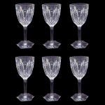 BACCARAT MALMAISON VARIANTE DO MODELO HARCOURT  SEIS MAGNIFICAS TAÇAS PARA VINHO DO PORTO  DO PRESTIGIADO MODELO MALMAISON UMA ELEGANTE VARIANTE DO HARCOURT QUE SURGIU NO CATÁLOGO DE 1910 DA MANUFATURA. AS TAÇAS BACCARAT MALMAISON DESTACAM-SE PELO EQUILÍBRIO ENTRE A IMPONÊNCIA DO CRISTAL LAPIDADO À MÃO E A LEVEZA DE SUAS LINHAS ESTRUTURAIS. ELAS TRAZEM UMA ESTÉTICA SÓBRIA E ARISTOCRÁTICA, TÍPICA DO ESTILO IMPÉRIO FRANCÊS. O BOJO (PARTE SUPERIOR): É ROBUSTO, PESADO E APRESENTA A FAMOSA LAPIDAÇÃO EM SEIS GOMOS OU FACETAS PLANAS E LARGAS (EXATAMENTE IGUAL AO MODELO HARCOURT). ESSAS FACETAS VERTICAIS FUNCIONAM COMO PRISMAS: QUANDO A LUZ INCIDE NO CRISTAL PURO, ELA É REFRATADA DE FORMA INTENSA, CRIANDO UM BRILHO GEOMÉTRICO MUITO CARACTERÍSTICO.  A HASTE (A PERNA DA TAÇA): AO CONTRÁRIO DA HARCOURT (QUE É CHEIA DE NÓS E ANÉIS), A HASTE DA MALMAISON É COMPLETAMENTE RETA, LISA E CILÍNDRICA. ELA NÃO POSSUI DETALHES ORNAMENTAIS, O QUE CONFERE À PEÇA UM VISUAL MUITO MAIS LIMPO, MODERNO E ANATÔMICO NA HORA DE SEGURAR. A BASE (O PÉ): TERMINA EM UM FORMATO SEXTAVADO COMO O CLÁSSICO MODELO HARCOURT, PLANO E LISO, OFERECENDO EXCELENTE ESTABILIDADE. FRANÇA, DEC. 1910. 13 X 6 CM