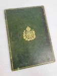 PASTA EM MARROQUIM TONALIZADO EM VERDE LAVRADO COM BRASÃO IMPERIAL BRASILEIRO REALÇADO EM OURO. PASTAS EM COURO VERDE COM O BRASÃO DO IMPÉRIO DO BRASIL ERAM USADAS POR ALTOS FUNCIONÁRIOS, MINISTROS E DIPLOMATAS PARA TRANSPORTAR, PROTEGER E APRESENTAR DOCUMENTOS OFICIAIS E CONFIDENCIAIS AOS GABINETES DE GOVERNO E AO PRÓPRIO IMPERADOR D. PEDRO II. O USO DO BRASÃO DA COROA NO COURO VERDE ERA ESTRITAMENTE CONTROLADO. APENAS MINISTROS DE ESTADO, DIPLOMATAS DE ALTO ESCALÃO E CONSELHEIROS POSSUÍAM AUTORIZAÇÃO PARA PORTAR ESSES MODELOS ESPECÍFICOS. PESAR DE SERVIREM AO GOVERNO BRASILEIRO, A MAIORIA DESSAS PASTAS DE LUXO ERA ENCOMENDADA E FABRICADA POR ARTESÃOS NA EUROPA, PRINCIPALMENTE EM PARIS E LONDRES, REFERÊNCIAS EM MARROQUINERIA FINA NO DEGUNDA METADE DO SÉCULO XIX. 18 X 12,5 CM
