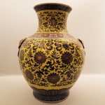 FAMILIA JAUNE - GRANDE E MAGNIFICO VASO DO PERÍDO REPUBLICANO (1912-1949) COM ESMALTES DA FAMILIA JAUNE E DESIGN DE ROLAGEM DE LÓTOS E ALÇAS EM FOMRA DE CABEÇA DE FERA MÍTICA (TAOTIE) MORDENTE DE ARGOLA. SELO APÓCRITO DO REINADO QIANLONG (QING QIANLONG NIAN ZHI). O SELO TEM ESTILO CALIG´RAFICO ZHUANGSHU COM PIGMENTO EM REBAIXO SOB O ESMALTE. A BASE AMPLA EXIBE UMA BORDA NÃO ESMALTADA NO PÉ DO VASO, ESPESSA E COM COLORAÇÃO TERROSA ESCURA. O ESMALTE TURQUESA COBRE TODA A PARTE INTERNA DA BASE DE MANEIRA UNIFORME ASSIM COMO NO INTERIOR DO PESCOÇO DO GARGALO. OS OARNAMENTOS NO CORPO DO VASO SÃO REALÇADOS EM OURO.  UM LARGO BARRADO EM ESMALTE LILÁS FAZ A TRANSIÇÃO ENTRE O GARGALO E BOJO. A PINTURA É DE EXCEPCIONAL QUALIDADE! CHINA, INICIO DO SEC. XX. 54 X 40 CMNOTA: Os esmaltes utilizados na porcelana Famille Jaune guardam segredos químicos intrigantes e carregam um forte simbolismo cultural da China Imperial. O vibrante fundo amarelo é um esmalte vítreo de baixa temperatura formulado à base de chumbo. Esse elemento funcionava como fundente, ajudando o esmalte a derreter e vitrificar de forma homogênea entre 750 C e 850 C.  A tonalidade amarela brilhante e opaca era obtida pela adição de óxido de antimônio (e às vezes ferro) misturado ao esmalte de chumbo, criando um pigmento conhecido historicamente como amarelo de Nápoles.  Diferente de outras porcelanas pintadas sobre o verniz branco já queimado, o esmalte da Famille Jaune era frequentemente aplicado diretamente sobre o biscuit (a massa de porcelana queimada apenas uma vez, sem nenhuma cobertura). Isso criava uma textura fosca e rica sob o esmalte amarelo. Em muitas peças, os artesãos entalhavam levemente os contornos dos desenhos na peça crua antes da primeira queima. Essas linhas serviam como barreiras físicas para impedir que o esmalte amarelo do fundo escorresse e invadisse os esmaltes coloridos (como o verde e o roxo) dos desenho. Na China, o amarelo era a cor sagrada do Imperador e da própria terra. Porcelanas com esmalte puramente amarelo eram de uso restrito da corte real, simbolizando poder supremo e sabedoria divina. O termo Famille Jaune foi cunhado por colecionadores franceses no século XIX (como Albert Jacquemart). Na verdade, os especialistas consideram esse estilo uma variação ou subcategoria da Famille Verte (família verde), já que ambas compartilham exatamente a mesma paleta de esmaltes coloridos para os desenhos, mudando apenas a cor de fundo.