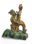 SANCAI  DINASTIA QING  - SEGUNDA METADE DO  SEC. XIX  ROOF TILE APRESENTANDO FIGURA DE IMORTAL MONTADO EM UMA AVE FENIX. TRATA-SE DE QIFENG XIANREN TAMBÉM CONHECIDO COMO "O IMORTAL CAVALGANDO UMA FÊNIX", UM ELEMENTO RECORRENTE NA ARQUITETURA CLÁSSICA CHINESA NA DINASTIA QING DO SÉC. XIX.  LOCALIZADO SEMPRE NA PONTA MAIS EXTERNA DA ARESTA DO TELHADO, ELE SERVE TANTO COMO UM ELEMENTO ESTÉTICO DE PRESTÍGIO QUANTO COMO UMA PEÇA ESTRUTURAL ESSENCIAL. SUA PRINCIPAL UTILIDADE PRÁTICA É SEGURAR E PRESSIONAR O PREGO DA PRIMEIRA TELHA DA PONTA. ISSO IMPEDE QUE OS FORTES VENTOS OU AS CHUVAS ARRANQUEM O TELHADO. ELE ATUA COMO O "CAPITÃO" DA FILEIRA. O NÚMERO DE ANIMAIS DECORATIVOS (COMO DRAGÕES, FÊNIX E LEÕES) QUE O SEGUEM DITA A IMPORTÂNCIA E A HIERARQUIA DO EDIFÍCIO. O SALÃO DA HARMONIA SUPREMA NA CIDADE PROIBIDA, POR EXEMPLO, OSTENTA O NÚMERO MÁXIMO PERMITIDO DE 10 ESTÁTUAS ATRÁS DO IMORTAL. A FIGURA ORIGINAL DESCRITA NO TRATADO ARQUITETÔNICO YANGZHOU FASHI ERA A PINJIA (, UMA CRIATURA BUDISTA COM CABEÇA HUMANA E CORPO DE PÁSSARO (BASEADA NA CRIATURA MÍTICA KALAVINKA).   COM A FORTE INFLUÊNCIA DO TAOISMO, O VISUAL MUDOU DE UMA CRIATURA HÍBRIDA BUDISTA PARA UM OFICIAL TAOISTA (CHAMADO DE ZHENREN OU IMORTAL) MONTADO DE LADO NAS COSTAS DE UMA FÊNIX.   A IMAGEM SE CONSOLIDOU NO FORMATO ATUAL, DO SEC. XIX ONDE O IMORTAL APARECE SENTADO DE FRENTE SOBRE A FÊNIX (QUE MUITAS VEZES SE ASSEMELHA A UM GALO NA ARTE POPULAR), TORNANDO-SE UMA FIGURA OFICIAL CATALOGADA NOS REGISTROS IMPERIAIS (QING HUI DIAN). COMO TUDO NA TRADIÇÃO CHINESA ENVOLVE UM SENTIDO, QIFENG XIANREN É UM AVISO DE PRUDÊNCIA E PRECAUÇÃO CONTRA A RUINA QUE PROVÉM DA GANÂNCIA (VIDE ABAIXO A LENDA DO RE MIN DE QI QUE INSPIROU O PERSONAGEM). NA EXTREMIDADE FRONTAL A FIGURA DE UM DRAGÃO ARCAICO CHILONG. CHINA, SEC. XIX 32 X 41 CMNOTA: O Rei Min de Qi  era um rei belicoso e ávido na conquista de terras- Diz a lenda que durante o Período dos Reinos Combatentes, este rei foi derrotado em batalha e encurralado à beira de um grande rio. Quando estava prestes a desistir, uma fênix gigante surgiu e o levou voando para longe, salvando sua vida. Na arquitetura, sua imagem no final do beiral representa a capacidade de transformar o azar em sorte e escapar de situações desesperadoras. Entretanto os arquitetos o colocam na ponta extrema do telhado justamente como um aviso contra a ganância: "mais um passo e você despenca". O EXPLENDOR DA CERÂMICA SANCAI: As peças de sancai, literalmente "peças de três cores", são figuras e vasos moldados em barro, com esmalte arrojado em tons de verde brilhante e âmbar sobre um fundo cor de palha. Mais raramente, azul ou marrom-púrpura também são adicionados. Essas peças estão tão profundamente enraizadas na história da arte chinesa que é difícil imaginar que foram redescobertas apenas no século XIX, quando túmulos da dinastia Tang foram acidentalmente desenterrados em Mangshan, perto de Luoyang, por topógrafos que construíam a ferrovia Longhai. Embora inicialmente ignoradas, algumas peças eventualmente chegaram ao antigo mercado de Liulichang, em Pequim, onde sua importância foi reconhecida pelos renomados filólogos Wang Guowei e Luo Zhenyu. O fascínio do sancai reside não apenas em suas cores brilhantes e formas esculturais expressivas, mas também em sua capacidade de evocar vividamente a vida deslumbrante, luxuosa e cosmopolita da dinastia Tang, proporcionando uma janela fascinante para essa era de ouro da China. Em coleções particulares e museus, as peças de sancai são destaques, com seus vasos de formatos exóticos de mais de mil anos atrás. AS ROOF TILES: As telhas Sancai são cerâmicas arquitetônicas tradicionais chinesas revestidas com uma técnica distinta de esmalte tricolor à base de chumbo.Originalmente introduzidas durante a Dinastia Tang (618907 d.C.) e altamente popularizadas durante as Dinastias Ming e Qing, essas telhas decorativas eram colocadas ao longo dos beirais e nas bordas dos telhados de templos, palácios e edifícios oficiais . Elas tinham dupla função: desviar estruturalmente a água da chuva e afastar espiritualmente os espíritos malignos.