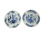 REINADO KANGXI  PAR DE PRATOS (DE UMA SEQUENCIA EM QUE FORAM  APRESENTADOS OUTROS QUATRO DO  MESMO CONJUNTO NOS DOIS LOTES ANTERIORES) EM PORCELANA CHINESA DO PERÍDO KANGXI (16621722)  DECORADOS EM ESMALTES AZUIS UNDERGLAZE.  UMA DAS ERAS DE MAIOR PRESTÍGIO E QUALIDADE NA HISTÓRICA DA PORCELANA AZUL E BRANCA DA CHJINA. COM DECORAÇÃO FLUIDA E ELEGANTE TEM NA ABA REMOS CONINUOS E SINUOSOS QUE SE ESTENDEM AO LONGO DE TODA A CIRCUNFERÊNCIA. ESSES RAMOS ALTERNAM ENTRE FOLHAS LANCEOLADAS DETALHADAS E BOTÕES DE FLORES ESTILIZADOS. NA TRADIÇÃO DA PORCLEANA CHINESA ESSES ARRANJOS DE TREPADEIRAS E FLORES NA BORDA NÃO SÃO MERAMENTE ESTÉTICOS, REMETEM A IDEIA DE CONTINUIDADE, LONGEVIDADE E RENOVAÇÃO CONSTANTE. A CALDEIRA É DECORADA EM PADRÃO BOGU QUE SIMBOLIZA VOTOS DE REFINAMENTO E BOA FORTUNA. ESTÃO NA CALDEIRA UM VASO CENTRAL QUE REMETE AS 100 ANTIGUIDADES, POUSADO SOBRE UM SUPORTE QUADRADO CLÁSSICO. O VASO É DECORADO COM ARRANJOS FLORAIS INDICANDO REFINAMENTO ACADÊMICO. FITAS FLUIDAS DITAS RIBBONS ENVOLVEM A MESA E O VASO ESSAS FITAS ESTÃO SEMPRE PRESENTES QUANDO SE APRESENTAM OS OBJETOS PRECIOSOS QUE INTEGRAM AS 100 ANTIGUIDADES. POSTERIORMENTE AOS VASOS ESTÁ UM TABULEIRO COM PADRÃO QUADRICULADO QUE REPRESENTA O JOGO MILENAR WEIGI UM DOS QUATRO TALENTOS ESSENCIAIS EXIGIDOS DE UM ERUDITO CHINÊS TRADICIONAL.  DELIMITANDO A CALDEIRA DA BORDA DUAS MOLDURAS DE LINHAS CONCÊNTRICAS DUPLAS. RARAMENTE SE ENCONTRARÃO DISPONÍVEIS SETS DE PORCELANA KANGXI COMO ESTE COM SEIS PRATOS  DE UM MESMO PADRÃO. CHINA, FINAL DO SEC. XVII OU INICIO DO XVIII. 23 CM DE DIAMETRONOTA:  Há 800 anos Marco Polo, trouxe da China para o ocidente a primeira peça de porcelana, um pequeno jarro verde acinzentado que está até hoje no tesouro da Basílica de São Marco em Veneza. Essa foi a semente da obsessão da Europa pelo Ouro Branco. No crepúsculo da DINASTIA MING, chegou à China em 1698 o Padre Jesuíta François Xavier d'Entrecolles. O declínio Ming sobreveio de uma crise causada pela corrupção, a exploração da classe dominante e desastres naturais durante anos sucessivos. Os rebeldes começaram a tomar o poder em algumas regiões e a dinastia chegou ao seu oficial fim com o suicídio do último imperador, Weizong. O poder passou então a nascente Dinastia Qing, que por 250 anos governou a China e sobre seu domínio a produção da porcelana Companhia das Indias atingiu seu apogeu em beleza e volume. Estima-se que 60 milhões de peças de porcelana foram exportadas para Europa nesse período. O Imperador QIANLONG governou o país por quase todo o sec. XVIII. Pouco antes do inicio desse grande reinado, ainda sob o período KANGSHI chegou a China o Padre DEntrecolles. Veio para salvar almas dos pagãos mas teve a sua própria alma arrebatada pela obsessão da porcelana. O ouro branco, encantou os europeus desde o primeiro leilão fruto da carga apreendida pelos holandeses de dois navios Portuguses. Era tão alto o preço da porcelana da China que um aparelho de jantar custava o equivalente ao valor de um pequeno palácio. Foi então que na Europa começou a busca da fórmula da composição e do processo para fabricação da porcelana. A princípio, julgaram que era feita a partir de conchas e casca de ovos moídos e tentaram reproduzir o efeito com esses matérias. Claro, tudo em vão porque a porcelana nada tinha a ver com esses elementos. O primeiro Imperador da Dinastia Qing foi Kangxi e este deu ordens de esconder, sob pena de morte, o processo de fabricação. O Padre DEntrecolles valeu-se dos chineses convertidos de Jingdezhen para descobrir aos poucos o processo. Um dia finalmente ele descobriu o segredo mais importante para obtenção da porcelana, em uma região remota chamada KAO-LING (COLINA ELEVADA) os chineses extraiam há séculos a argila chamada caulim que era o principal elemento constituinte da louça da China. O resto, as proporções, o modo de fazer, de decorar e a queima ele cuidou em aprender gradativamente. Em 1712 o Padre DEntrecolles escreveu para França relatando suas descobertas e descrevendo em minúcias o processo de fabricação. Dessa forma um segredo milenar foi revelado a Europa ensandecida pela porcelana e sua capacidade de trazer riquezas além de qualquer sonho aos homens. Paralelamente na Europa, Augusto II, chamado O FORTE, aprisionou em seu castelo um jovem aprendiz chamado BOTTEGER, que se gabava de ser alquimista, e o ameaçou de pena de morte se não conseguisse desvendar o processo para a fabricação. Cinco anos BOTTEGER esteve preso realizando experimentos sistemáticos até chegar por seu próprio mérito à fórmula da porcelana. Embora não tenha sido um método muito ortodoxo, funcionou. Surgiu a manufatura de Meissen. Nessa mesma época na China, LANG TINGJI, foi nomeado pelo Imperador KANGXI, supervisor de porcelana nos fornos de Jingdezhen. A intenção do Imperador era a de recriar as famosas porcelanas monocromáticas do período Ming do SEC. XIV. Os chineses tem essa particularidade, um respeitoso culto aos ancestrais e suas conquistas. Edmund de Waal em seu livro O Caminho da Porcelana: A jornada de Uma Obsessão (recomendo muitíssimo) referencia assim essa respeitosa paixão pela memória dos ancestrais: Esse pode ser o ano em que alguém encomenda a fabricação de turíbulos que se parecem muito com os turíbulos feitos há trezentos anos. Esses por sua vez foram feitos para aludir bronzes de 900 anos atrás. Assim a devoção atravessa os séculos e as gerações. A porcelana chinesa antiga ainda traz encantamento por sua beleza, sua coloração branca azulada e a magnífica decoração. Não por acaso, cada peça de porcelana Companhia das Índias que nos chega à mão é tratada com reverência e devoção não apenas por ser fruto do trabalho do oleiro que lhe deu forma e a decorou, mas por ser produto de 5000 anos de uma cultura extraordinária e única. AS CEM ANTIGUIDADES O PRINCIPIO DAS COISAS:As "Cem Antiguidades" (Baigu ou Po-ku) é um famoso tema decorativo da arte chinesa que reúne emblemas de boa sorte, sabedoria e erudição, refletindo os ideais da classe letrada tradicional. O motivo não representa exatamente cem objetos literais, mas sim uma rica coleção de itens associados à cultura, ao estudo e à filosofia na China antiga. Das cem antiguidades se originaram tudo que existe no mundo. Objetos de Estudo: Pincéis, blocos de tinta, papel e pedras de amolar tinta (os quatro tesouros do letrado).Artes e Passatempos: Instrumentos musicais, tabuleiros de xadrez chinês, livros e rolos de pintura ou caligrafia. Rituais e Símbolos: Vasos de bronze arcaicos, queimadores de incenso, cetros ruy de prosperidade e recipientes rituais que homenageiam os antepassados. Esse repertório visual consolidou-se fortemente durante a dinastia Qing (16441911) e era aplicado em porcelanas, pinturas e painéis. Demonstra a busca por virtude, refinamento intelectual e o respeito contínuo aos ancestrais. Cada objeto funciona como um símbolo ou enigma visual que deseja vida longa, paz, felicidade e riqueza para o lar.
