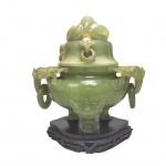 GRANDIOSO INCENSÁRIO RITUALISTICO DE ANÉIS SOLTOS DITO FANGDING  ESCULPIDO EM JADE E ACOMODADO SOBRE BASE EM MADEIRA. DE IMPRESSIONANTE DIMENSÃO TEM ALÇAS LATERAIS COM FIGURAS DE DRAGÕES  COMPLETOS MORDENTES. A TAMPA TEM PEGA COM FIGURA DE UM DRAGÃO CHILONG. O CONJUNTO REPOUSA SOBRE TRÊS PÉS COM GARRAS E NA JUNÇÃO DAS PERNAS COM O BOJO DO INCENSÁRIO TRES CABEÇAS DE TAOTIE CRIATURA MÍSTICA ASSOCIADA A FUNÇÃO DE GUARDIÕES. NOTE QUE OS ANÉIS PENDURADOS NAS ALÇAS E EM TORNO DAS TAMPAS MOVIMENTAM-SE LIVREMENTE ISSO PORQUE SÃO ESCULPIDOS EM UM ÚNICO BLOCO MACIÇO DE PEDRA DO QUAL SE ORIGINA TODO O CONJUNTO DO INCENSÁRIO.UMA PEÇA COMO ESSA PELA COMPLEXIDADE DA ESCULTURA E DUREZA DA PEDRA ENVOLVE MESES OU ATÉ ANOS DE TRABALHO UTILIZANDO BROCAS MANUAIS E AREIA ABRASIVA PARA ESCULPIR E CAVAR NA PEDRA. O FORMATO TRIPOIDAL É HERDADO DOS ANTIGOS BRONZES RITUAIS CHINESES CHAMADOS DING QUE SIMBOLIZAVAM AUTORIDADE E ESTABILIDADE. EIS UMA OBRA EM QUE A PRÓPRIA PEDRA PARECE SOPRAR VIDA E POESIA. ESCULPIDO NO SOPRO DA PACIÊNCIA A PARTIR DE UM ÚNICO E RARO BLOCO MINERAL, ESTE INCENSÁRIO CARREGA A SERENIDADE DOS ANTIGOS RITUAIS: A FUMAÇA PERFUMADA SUBIA SUAVEMENTE PELAS PÉTALAS DO TOPO, ENQUANTO AS ALÇAS BALANÇAVAM COMO UM SUSSURRO DE ELEGÂNCIA NOS SALÕES DA NOBREZA ORIENTAL. CHINA, FINAL DO SEC. XIX OU INICIO DO XX. 26 X 24 CM 3520 GNOTA: Incensários de jade carregam  séculos de tradição espiritual, status social e maestria técnica. Na China queimar incensos em vasos de jade purifica o ambiente e atraem boas energias. Durante as dinastias Ming e Qing peças luxuosas de jade eram exclusivas dos altares imperiais ou de famílias nobres.