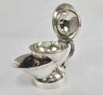 PRATA DE LEI INGLESA  REINADO GEORGE V - CURIOSO SHAVING SCUTTLE (CANECA DE BARBEAR) EM PRATA DE LEI COM MARCAS PARA CIDADE DE LONDRES LETRA DATA 1920, PRATEIRO MAPPIN & WEBB.. DE FEIÇÃO ART DECO FOI UM ITEM DE LUXO INDISPENSÁVEL PARA O BARBEAR CLÁSSICO TRADICIOANAL. O BOCAL QUE SE PROJETA NA PARTE FRONTAL DO CANECO SERVE PARA DESPEJAR AGUA FERVENTE DIRETAMENTE NO REFSERVATÓRIO INFERIOR. ISSO MANTÉM A PEÇA AQUECIDA DURANTE TODO O PROCESSO DE BARBEAR. O BOWL SUPERIOR COM TAMPA BASCULANTE É ONDE SE COLOCAVA O SABÃO SÓLIDO DE BARBEAR. O CALOR DA ÁGUA FERVENTE QUE VEM DE BAIXO DERRETIA LEVEMENTE O SABÃO MANTENDO A ESPUMA AQUECIDA E CONFORTÁVEL PARA O ROSTO. FUROS NA BASE SUPERIOR DRENAVAM O EXCESSO DE ÁGUA DO PINCEL DE BARBEAR MANDANDO=A DE VOLTA PARA O RESERVATÓRIO. UMA ALÇA LATERAL PERMITIA AO USUÁRIO MANIPULAR COM FACILIDADE O ARTEFATO. INGLATERRA, INICIO DO SEC. XX. 18 CM DE COMPRIMENTO. 240 G. NOTA: O s potes de barbear foram petenteados no sec. XIX durante a era Vitoriana. na Inglaterra. Naquela época as casas não tinham água quente nas torneiras. O pote permitia que o usuário levasse a água fervendo diretamente da cozinha para o toilette. . No ´seculo XIX as barbearias públicas eram focos de  infecções d epele e fungos que causavam uma reação infecciosa conhecida como coceira de barbeiro. . Assim os homens endinheirados compravam seus próprios pincéis e potes de barbear personalizados. Muitos os guardavam em prateleiras numeradas nas barbearias,eram os "clubes de barber". Ter uma caneca de barbear em prata de lei era um grande símbolo de riqueza e masculinidade. O uso desses potes despencou drasticamente ainda na primeira metade do sec. xx pela invenção ocmbinada dos cremes de barbear e o encanamento de água quente. nas residências urbanas.