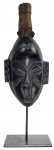 MÁSCARA FACIAL RITUAL GURO  COSTA DO MARFIM/GANA. MÁSCARA ANTROPOMÓRFICA DO POVO GURO. OLHOS SEMICERRADOS AMENDOADOS, A MÁSCARA É O ELEMENTO CENTRAL DO RITUAL E DA DANÇA ZAOULI, UMA MANIFESTAÇÃO CULTURAL TÃO RICA QUE FOI DECLARADA PATRIMÔNIO CULTURAL IMATERIAL DA HUMANIDADE PELA UNESCO.. ÁFRICA, INICIO DO XX. 35 CM DE ALTURA (NÃO CONSIDERANDO A ALTURA DO SUPORTE EM METAL QUE ACOMPANHA A PEÇA)NOTA: As máscaras rituais das etnias Guro e Baule desempenham papel social e espiritual essencial. A máscara representa a figura idealizada de uma jovem de extrema beleza chamada Djela Lou Zaouli (traduzido como "Zaouli, a filha de Djela" ou "A filha do leão"  : O ritual é realizado em funerais, celebrações e grandes festas. O povo Guro acredita que a presença da máscara atrai prosperidade, paz, união e produtividade para a aldeia. Embora a máscara homenageie a beleza feminina, o dançarino que a veste é sempre um homem iniciado no ritual. performance é conhecida informalmente como "a dança mais impossível do mundo". O dançarino move os pés e as pernas em uma velocidade ultrarrápida, sincronizado com os tambores, enquanto mantém a parte superior do corpo inteiramente imóvel.