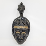 MASCARA CAPACETE RITUALÍSTICA  COM FEITIO DE FIGURA FEMININA  POVO SENUFE  COSTA DO MARFIM  APRESENTA TRAÇOS MARCANTES DE IDEALIZAÇÃO ESTÉTICA AFRICANA  OLHOS AMENDOADOS E SEMICERRADOS, ESCARIFICAÇÕES FACIAIS GEOMÉTRICAS (MARCAS DE PRESTÍGIO E PERTENCIMENTO), PESCOÇO ANELADO (SÍMBOLO DE BELEZA, PROSPERIDADE E FARTURA) E PENTEADO ELABORADO. AS MÁSCARAS COM FIGURAS FEMININAS NO TOPO SÃO SÍMBOLOS DE FERTILIDADE, ANCESTRALIDADE E SABEDORIA MATRIARCAL. NAS SOCIEDADES SECRETAS TRADICIONAIS DA ÁFRICA OCIDENTAL, COMO A SOCIEDADE PORO OU SANDOGO, A FIGURA DA MULHER REPRESENTA A FIGURA DA MÃE ANCESTRAL QUE PROTEGE A COMUNIDADE, ABENÇOA A COLHEITA E INTERCEDE JUNTO AOS ESPÍRITOS DA NATUREZA. COSTA DO MARFIM, INICIO DO SEC. XX. 38 CM DE ALTURANOTA: Nas sociedades tradicionais da África Ocidental, as máscaras ritualísticas e os elmos esculpidos desempenham um papel central no diálogo entre o mundo visível e o plano dos ancestrais. Elas eram utilizadas em cerimônias de iniciação, ritos funerários de passagem e festivais de celebração da colheita ou da fertilidade. O dançarino que a vestia deixava de ser um indivíduo comum para personificar a própria entidade ou espírito protetor da tribo.