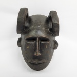 MÁSCARA RITUAL BAOULÉ - COSTA DO MARFIM - MÁSCARA ANTROPOMÓRFICAS COM CHIFRES CURVADOS PARA FRENTE E PARA BAIXO NO TOPO DA CABEÇA REPRESENTANDO A FORÇA ANIMAL (FREQUENTEMENTE ASSOCIADA AO CARNEIRO OU AO BÚFALO SEVALGEM) . NA ESCULTURA DE MÁSCARAS DA ÁFRICA OCIDENTAL OS CHIFRES SIMBOLIZAM A CONEXÃO  ENTRE O MUNDO HUMANO E A NATUREZA DOS ESPÍRITOS ANCESTRAIS. AS MEIA LUAS ESCULPIDAS EM RELEVO NAS TEMPORAS E NAS BOCHECHAS E TÊMPORAS REFLETEM MARCAS TRADICIOANIS  DE ESCARIFICAÇÃO OU REPRESENTAÇÕES ESTILIZADAS DE PENTEADOS TRADICIONAIS.  OS OLHOS ESTREITOS E SEMICERRADOS O NARIZ RETO E A BOCA SERENA INCORPORAM IDEAIS CULTTURAIS DE PAZ INATERIOR, SERENIDADE E  SABEDORIA ESPIRITUAL. É UMA MASCARA DE PERFORMANCE RITUAL E DANÇAS. UTILIZADA EM CERIMONIAS GOLI OU MBLO (BAULE) REALIZADAS NOS FESTIVAIS DE ENTRETENIIMENTO, CELEBRAÇÃO DA COLHEITA, HOMENAGEM A ANCIÃOS RESPEITADOS OU RITUAIS FÚNEBRES. OS CHIFRES SÃO ROBUSTOS E PLENAMENTE INTEGRADOS NA ESCULTURA FORAM ESCULPIDOS DE UM SÓ BLOCO DE MADEIRA. COSTA DO MARFIM, INICIO DO SEC. XX. 28 CM DE ALTURA