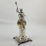 PALITEIRO NETUNO - MAGNÍFICO PALITEIRO DE MESA DE BANQUETE  EM PRATA DE LEI. O DEUS DOS MARES SURGE COROADO, EMPUNHANDO SEU TRIDENTE E POSICIONADO A FRENTE DE UMA CONCHA DE VIEIRA SUTENTADO POR UM PEDESTAL EM FACETAS COM BASE APRESENTANDO ORNAMENTOS FLORAIS ,ASSENTE SOBRE PÉS DE GARRA. MARCAS DE CONTRASTE P COROADO (CIDADE DO PORTO) E PRATEIRO CAETANO RODRIGUES DE ARAUJO ENSAIADOR DA CIDADE DATAVEL DA DECADA DE 1840 (MOITINHO PAG. 230). TRATA-SE DA REPRESENTAÇÃO DO DEUS NETUNO, REI DOS MARES. ESSE PALITEIRO FAZ PARTE DA SÉRIE SURGIDA NO INÍCIO DO SEC. XIX COM PERSONAGENS MITOLÓGICOS E SÃO EXTREMAMENTE COLECIONÁVEIS NO BRASIL E EM PORTUGAL. PORTUGAL, SEC. XIX, 22 CM DE ALTURA.NOTA: A história dos paliteiros, como objetos de coleção e decoração, está ligada à evolução dos hábitos sociais e à apreciação de objetos antigos e requintados. Os palitos de dente surgiram como objetos funcionais, utilizados para higiene bucal após as refeições. Inicialmente, eram simples e feitos de materiais como madeira ou osso. Com o passar do tempo, os palitos evoluíram para objetos mais elaborados, com designs variados, feitos de materiais como prata, ouro e outros metais preciosos. Eram objetos pessoais que usados tanto na residência de seu possuidor quanto levados a banquetes ou refeições fora de sua casa quanto mais ostensivos ou preciosos mais indicavam a riqueza e importância social de seu possuidor. Com o tempo os palitos passaram a ser apresentados em paliteiros levados a mesa para servir a todos os convivas. Evoluíram para objetos mais elaborados, com designs variados, feitos de materiais como prata, porcelana e outros metais preciosos. No Brasil por herança de Portugal os paliteiros assumiam formas decorativas e elaboradas para compor com elegância as mesas. Sendo geralmente confeccionados em prata de lei. Esses paliteiros adornados por esculturas, flores, deuses, pássaros continham orifícios onde os palitos de marfim ou espinhos de laranjeira e limoeiro eram inseridos para o uso. Embora paliteiros existissem em outros locais, nenhum lugar do mundo teve tanta paixão por colecionar e fabricar paliteiros figurativos em prata quanto Portugal e o Brasil. Tornou-se uma especialidade artística da ourivesaria do Porto e de Lisboa. Historiadores de arte apontam que essa profusão de modelos detalhados (com figuras humanas, deuses e animais) é um fenômeno cultural quase exclusivo do mercado luso-brasileiro. A figura de Netuno (Rei dos Mares) pertencia a séries de personagens mitológicos criadas pelos ourives que frequentemente faziam pares. Era muito comum que as famílias ricas comprassem dois paliteiros coordenados para equilibrar a decoração simétrica das grandes mesas: um representando Netuno e outro representando sua esposa, a deusa Anfitrite (Rainha dos Mares)Modelos similares aos existentes no acervo do Museu Imperial eram conhecidos desde o final do século XVIII em Portugal, chegando ao Brasil por influência, e tendo seu auge no século XIX. Os prateiros europeus produziam paliteiros com formas diversas e elaboradas. Personagens históricos, como Vasco da Gama e Napoleão, animais, como pavões e pássaros, frutas como romãs e uvas e flores em ramos e buquês eram frequentes. No Brasil, alguns temas sofreram influência nacional, frutas como abacaxis e cajus, personagens como figuras representando indígenas estilizados, como este exemplar do acervo Museu Imperial, além de elementos africanos, foram representados nos paliteiros utilizados aqui, produzidos principalmente no Rio de Janeiro e Bahia.