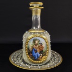 BACCARAT  LUXUOSA GARRAFA DE TOUCADOR E SEU PRESENTOIR DA ESCOLA DE BACCARAT (CRISTAL DA MANUFATURA E ATELIER DE DECORAÇÃO) ESTILO EPOCA SEGUNDO IMPERIO FRANCÊS (ENTRE 1855-1880). TODO O CORPO DA GARRAFA E O PRESENTOIR É DECORADO COM ESCUDELLAR CORRUGADAS ENTREMEADOS POR PÉROLAS RELEVADAS EM ESMALTE OPALESCENTE (BEADING). ESTAS PÉROLAS SÃO FEITAS DE ESMALTES SOPRADOS APLICADOS A QUENTE UM TRABALHO QUE EXIGE EXÍMIA APTIDÇÃO ARTISTICA.BARRADOS E FRISOS EM OURO. A GARRAFA TEM RESERVA COM EXUBERANTE PINTURA PASTORAL GALANTE AO ESTILO DE WATTEAU E LANCRET  EXECUTADA EM ESMALTES MANUAIS. MEIAS PÉROLAS REMATADAS EM OURO EMOLDURAM A PINTURA QUE TEM ASSINATURA DO ARTISTA. A BASE DO CRISTAL TEM UM PONTIL DE CORTE E POLIMENTO UM ACABAMENTO QUE DENOTA SUA QUALIDADE EXTRA. DESTINADO A COMPOR UM  SERVIÇO DE TOUCADOR DE LUXO DA ALTA BURGUESIA OU ARISTOCRACIA FAZ PARTE DA CATEGORIA DOS FRASCOS GALANTES INSPIRADOS NA PINTURA ROCOCÓ FRANCESA DO SEC. XVIII. FRANÇA, MEADOS DO SEC. XIX. 21 CM ALTURA (GARRAFA) E 18 CM DE DIAMETRO (PRATO).
