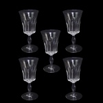 BACCARAT POLIGNAC   COM SELO DA MANUFATURA   ORIGINALMENTE ENCOMENDA DO GOVERNO FRANCÊS (PRESIDENTE RENÉ COTY) PARA O BANQUETE OFICIAL OFERECIDO EM HOMENAGEM A RAINHA ELIZABETH II NA GALERIA DOS ESPELHOS DO PALÁCIO DE VERSALHES EM 9 DE ABRIL DE 1957. RÉGIO CONJUNTO COM CINCO TAÇAS PARA ÁGUA EM CRISTAL DO MODELO POLIGNAC DA BACCARAT. APRESENTA LAPIDAÇÕES VERTICAIS ESPESSAS E PROFUNDAS (ORGUE BEVEL CUTS) QUE SAEM DA HASTE E SOBEM PELO BOJO. O DETALHAMENTO GEOMÉTRICO CRIA UM VISUAL ROBUSTO QUE SIMULA UM CÁLICE MODERNO, CONTRASTANDO COM A SUAVIDADE DA BORDA SUPERIOR LISA. FOI BATIZADO EM HOMENAGEM À DUQUESA DE POLIGNAC, FIGURA HISTÓRICA CONHECIDA POR SEU GOSTO REFINADO E PROXIMIDADE COM A RAINHA MARIA ANTONIETA. FRANÇA, DEC. 1950. 16 CM DE ALTURA.NOTA: O modelo foi criado exclusivamente para servir a Rainha Elizabeth II e o Príncipe Philip em sua visita oficial à França em 1957. Ele decorou a mesa do banquete na Galeria dos Espelhos no Palácio de Versalhes. O presidente francês René Coty encomendou o design para impressionar a monarca com a modernidade do cristal francês. Seus cortes verticais profundos funcionam como prismas que refletem a luz das velas, criando um brilho único na mesa. Cada taça exigia o trabalho de vários artesãos altamente qualificados, conhecidos como Meilleurs Ouvriers de France.do: Devido à lapidação profunda, as taças são notavelmente mais pesadas que os modelos tradicionais. O nome celebra a Duquesa de Polignac, que foi a amiga mais íntima e favorita da rainha Maria Antonieta. As peças produzidas antes de 1936 não tinham logotipo gravado, mas como o Polignac nasceu nos anos 1950, todas as peças originais trazem a marca circular jateada da Baccarat na base.
