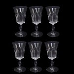 BACCARAT POLIGNAC   COM SELO DA MANUFATURA  IGENTICAS AS OFERTADAS NO LOTE ANTERIOR.  .ORIGINALMENTE ENCOMENDA DO GOVERNO FRANCÊS (PRESIDENTE RENÉ COTY) PARA O BANQUETE OFICIAL OFERECIDO EM HOMENAGEM A RAINHA ELIZABETH II NA GALERIA DOS ESPLEHOS DO PALÁCIO DE VERSALHES EM 9 DE ABRIL DE 1957. RÉGIO CONJUNTO COM SEIS TAÇAS PARA VINHO BRANCO EM CRISTAL DO MODELO POLIGNAC DA BACCARAT. APRESENTA LAPIDAÇÕES VERTICAIS ESPESSAS E PROFUNDAS (ORGUE BEVEL CUTS) QUE SAEM DA HASTE E SOBEM PELO BOJO. O DETALHAMENTO GEOMÉTRICO CRIA UM VISUAL ROBUSTO QUE SIMULA UM CÁLICE MODERNO, CONTRASTANDO COM A SUAVIDADE DA BORDA SUPERIOR LISA. FOI BATIZADO EM HOMENAGEM À DUQUESA DE POLIGNAC, FIGURA HISTÓRICA CONHECIDA POR SEU GOSTO REFINADO E PROXIMIDADE COM A RAINHA MARIA ANTONIETA. FRANÇA, DEC. 1950. 13 CM DE ALTURA.NOTA: O modelo foi criado exclusivamente para servir a Rainha Elizabeth II e o Príncipe Philip em sua visita oficial à França em 1957. Ele decorou a mesa do banquete na Galeria dos Espelhos no Palácio de Versalhes. O presidente francês René Coty encomendou o design para impressionar a monarca com a modernidade do cristal francês. Seus cortes verticais profundos funcionam como prismas que refletem a luz das velas, criando um brilho único na mesa. Cada taça exigia o trabalho de vários artesãos altamente qualificados, conhecidos como Meilleurs Ouvriers de France.do: Devido à lapidação profunda, as taças são notavelmente mais pesadas que os modelos tradicionais. O nome celebra a Duquesa de Polignac, que foi a amiga mais íntima e favorita da rainha Maria Antonieta. As peças produzidas antes de 1936 não tinham logotipo gravado, mas como o Polignac nasceu nos anos 1950, todas as peças originais trazem a marca circular jateada da Baccarat na base.