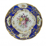 DOM PEDRO II - SERVIÇO DE CAÇA - MAGNÍFICO PRATO EM PORCELANA FRANCESA, ABA AZUL ROYAL E DOURADO; QUATRO RESERVAS, DUAS A DUAS, COM PÁSSAROS E FLORES; CALDEIRA COM RAMO DE FLORES EM POLICROMIA E ARABESCOS DOURADOS. ESSE APARELHO FOI OFERECIDO A DOM PEDRO II PELO IMPERADOR DA FRANÇA NAPOLEÃO III ENTRE 1852 E 1870. REPRODUZIDO À PÁGINA 211 DO LIVRO "LOUÇA DA ARISTOCRACIA NO BRASIL", POR JENNY DREYFUS. FRANÇA, SÉC. XIX. 22,5 CM DE DIÂMETRO.NOTA: Como leiloeiros muitas vezes nos deparamos com a surpresa de nossos clientes principalmente na sala de leilão com o fato de um objeto da Família Imperial Brasileira ser levado à hasta pública. A pergunta recorrente é: Como esse objeto pode ter vindo parar aqui não teria de estar em um museu?. Por isso resolvi escrever um pouco sobre o desfecho da memória física da família Imperial Brasileira após o golpe republicano. Passados 129 anos da fatídica madrugada chuvosa e melancólica em que a Família Imperial embarcou para seu exílio na Europa em 17 de novembro de 1889 rememoramos um fato que aprendemos na escola, Dom Pedro II não pede indenização por suas propriedades perdidas, valores, haveres, apenas dirige ao governo provisório o pedido de um saco com terra do Brasil para pousar sua cabeça quando morresse. Tudo ficou para trás, o elo perdido da monarquia era um corpo insepulto nos corredores e aposentos dos palácios imperiais cheios de suas mobílias e alfaias. A última coisa que os golpistas desejariam era preservar essa memória em um museu. O novo sistema de governo sem legitimidade tratou de tentar varrer a honrada memória de Dom Pedro II e de sua família. Assim rapidamente organizou dezenas de leilões públicos para dar cabo da acusadora lembrança do regime imperial. Tomo a liberdade de transcrever alguns trechos Litiere C. de Oliveira a propósito dos leilões dos paços imperiais: O nono leilão realizado no Paço de São Cristóvão, realizado em 3 de outubro de 1890, começou com uma novidade que ainda hoje não é praticada em nenhum leilão de arte, que foi a venda antecipada, "por conveniência", de 28 lotes, não se sabe a quem nem o motivo! Entre as peças vendidas, destacamos: uma bela pintura a óleo sobre tela, "Vista de Veneza" com moldura veneziana, autor não revelado; três quadros pequenos e uma aquarela; um quadro "Paisagem", o.s.t. de artista ignorado; quatro telas, pontes "St. Pierre et neuf á Toulouse", "Hospício de la Grave" e "Eglise des Jesuites", Toulouse; uma pintura o.s.t. "Claustro de um convento" por M.C., 1843; uma pintura o.s.t. "Peregrino" por L. Moureaux; uma mesa e 12 cadeiras de mogno com assento e encosto de palhinha; duas mesas de mogno para jogo; quatro castiçais de Cristofle; seis antigas cadeiras de jacarandá esculturadas; secretária de mogno com guarnições de bronze dourado e fundo de espelho; outros móveis e diversos quadros e aquarelas. Segundo Francisco Marques dos Santos, "o leilão do Imperador foi como um destes grandes leilões modernos; o entusiasmo não arrefeceu, muito embora não fosse a São Cristóvão um número considerável de pessoas de destaque, justamente aquelas timoratas e outras que imaginavam se comprometer e algumas que, sendo hostis ao novo estado de coisas, não queriam arrostar os desordeiros que espionavam a casa, por própria conta ou de terceiros, fazendo, não raro, achincalhe ao antigo regime. Nesse leilão o que mais se via eram senhoras, formando grupo maior do que em dias anteriores. O leilão atravessou os aposentos particulares do Imperador e aquela gente estava na volúpia de devassar, ver os recantos onde vivia uma família arrebatada de sua Pátria pelo sopro tempestuoso dos acontecimentos políticos. No decorrer do leilão todos os móveis com a coroa imperial ou iniciais dos ex-imperadores adquiriram preços muitas vezes maiores do que a avaliação que lhes fizeram..."Esse nono leilão também ficou marcado por um fato inusitado e talvez inédito na leiloaria brasileira. Ao apregoar um piano de cauda (lote 1747), em caixa de jacarandá e tuia, com escultura e filetes dourados, fabricado por Chickering e comprado pelo Sr. Antônio Rezende por 2:000$000 (US$ 1.080), o leiloeiro Virgílio sentou-se ao piano e executou uma música. O referido piano está hoje no Museu Histórico Nacional. O décimo leilão foi realizado em 7 de outubro e se destacou pela acirrada disputa pelo dormitório da Imperatriz. Somente a cama de jacarandá com coroa esculturada e colchão de crina (lote 2001), foi vendida por preço recorde: 7:000$000 (três mil, setecentos e oitenta Dólares). Enquanto isso a cama onde dormia o Imperador (lote 1980), por ser um móvel modesto, sem coroa, brasão ou iniciais, alcançou apenas o preço de 190$000 (102 Dólares)! Era uma sólida cama de mogno e érable, com acolchoado de crina vegetal e lastro de palhinha. O filho e a governanta alemã do comprador afirmaram, tempos depois, que a cama foi destruída pelos cupins e jogada fora! Outros destaques desse leilão foram: cama de jacarandá que pertenceu à Princesa Isabel quando solteira, com escultura e coroa, comprada pelo Comendador Antônio Rezende por 3:100$000 (US$ 1.673), e que depois foi vendida no leilão do Conde Sebastião de Pinho ao Dr. Castro Maia, cujo filho doou ao Museu Imperial; um lavatório de jacarandá com esculturas, bronze e tampo de mármore (lote 1983), adquirido pelo Sr. A. Rezende por 5:000$000 (US$ 2.700); guarda-roupa de D. Pedro II (lote 1984) vendido por 2:000$000 (US$ 1.512); cadeira de repouso do Imperador (lote 1885) de jacarandá, com escultura, coroa e iniciais comprada pelo Comendador A. Rezende por 3:100:000 (US$ 1.674); entre outros. Realizado no dia 10 de outubro, o décimo primeiro leilão compreendeu os lotes 2001 a 2345, com aproximadamente 650 peças. Até aquele momento os leilões tinham atingido 400 contos de Réis, cerca de 215 mil Dólares, valor muito superior à avaliação inicial de 90:000$000, e ainda faltavam mais de dez pregões. Esse leilão era constituído de objetos que tinham sobrado do dormitório dos imperadores, das salas 40 e 41, galeria, sacristia e tribuna. Entre as peças leiloadas estavam: um oratório de jacarandá esculturado e guarnecido de cornalinas, lápis lazuli e figuras de bronze (lote 2007) que foi comprado pelo Dr. Faro por 3:000$000 (US$ 1.620); uma secretária de bois-rose com placas de porcelana de Sèvres e guarnições de bronze dourado (lote 2135) adquirida pelo Barão de Itacurussá por 7:000$000 (US$ 3.800); guarda roupa de jacarandá com guarnições de bronze dourado, coroa e espelho francês (lote 2034) alienado por 5:000$000 (US$ 2.700) ao Sr. Antônio Resende; uma mobília de jacarandá com 11 peças (lote 2236) vendida ao Sr. Goulart e outros móveis, ricas pinturas, porcelanas, esculturas, muitos objetos de decoração e bibelots, quase todos esses lotes a preços irrisórios. Ao final do décimo primeiro leilão, o último realizado no interior do Paço de São Cristóvão, relata Marques dos Santos: "Depois do leilão da galeria do 2º andar, desceu o leiloeiro ao pavimento térreo, onde estava a capela e suas dependências, que deviam imediatamente desaparecer, para dar lugar ao salão cenográfico do Congresso. O singelo e gracioso templo, concepção de Manoel de Araújo Porto Alegre, ostentava na frontaria Ecce Agnus Dei. Abrangia a nave propriamente dita e a sacristia, em dois compartimentos, além da tribuna, onde o pregão do leiloeiro emudeceu! Ali estacou! Naquele lugar onde tanta gente fora batizada, acrescendo ao nome o apelido de do Paço, onde tanta vez rezaram os Imperadores, em horas alegres e amargas! Já que falamos em capela: ainda vemos em São Cristóvão, no primeiro andar, ao Torreão do Norte, o local onde ficava o altar privado dos Imperadores, cuja abóboda, pintada de azul celeste, deixa ver em pequeno céu, mimosas estrelinhas de prata! Que recordações trazem!" O décimo segundo leilão foi realizado em uma das cocheiras do Paço de São Cristóvão, com os objetos não licitados, não retirados ou que não foram incluídos nos leilões anteriores. Esse leilão foi realizado no dia 20 de outubro, abrangendo 155 lotes. Foram leiloados quadros a óleo, ricos espelhos, estantes de jacarandá e de mogno, porcelanas valiosas, cristais, molduras de quadros que tinham ido para a Europa (!), um telescópio que ficava no terraço do Paço, alguns móveis e outros objetos. O décimo terceiro leilão foi realizado no dia 10 de novembro de 1890 abrangendo as benfeitorias da Quinta da Boa Vista, assim relatado por Francisco Marques dos Santos: Foi arrematante dessas benfeitorias o próprio governo. Supomos que foi o Comendador Bethencourt da Silva quem comprou por 320:000$000, como representante do Ministério do Interior e Justiça as casas ali existentes, habitadas pelos empregados e protegidos da família Imperial, desde o tempo de Dom João. Essa operação foi considerada bastante vantajosa. Segundo a Gazetilha do Jornal do Commércio de 12 de novembro, valia perto de 300:000$000 só a casa do mordomo ou Quinta da Joana, como era conhecida a grande habitação próxima ao portão da Estrada de Ferro, na então Rua Duque de Saxe. Era solidamente construída, com vastas acomodações para família, abundância de água, gaz, aparelhos e magnífico terreno. O edifício que o Imperador construíra de seu bolso para escola mista diurna e noturna, destinada aos filhos dos moradores da Quinta e seus arredores, fora reedificado em 1883 e custara 60 contos de réis. Arrematou-a o Ministério da Instrução Pública por 41:000$000. Cumpre, aliás, notar que o governo sempre fez bom negócio naquilo que comprou, pertencente ao Imperador! Antes dos leilões da Fazenda Imperial de Santa Cruz, um outro foi realizado nas cocheiras do Paço da Cidade, no dia 5 de dezembro, lotes 1 a 14, compreendendo as últimas carruagens que se achavam espalhadas por diversas cocheiras particulares. O destaque foi um rico coche de gala com lanternas de cristal, guarnições de bronze e armas imperiais. Também foi vendido nesse leilão o carro mortuário, com coroa imperial que, entre outros nomes importantes, fez o enterro do General Osório e do Marques do Paraná. Quando a DARGENT LEILÕES leva a pregão objetos como o desta coleção ligados ao cotidiano da Família Imperial Brasileira sempre busca justamente o contrário do que o regime republicano tentou com a venda dos objetos imperiais. Não buscamos esconder, apagar, esmaecer a augusta memória de Dom Pedro II, mas sim exaltar a figura de um patriota e do homem que construiu as bases para o crescimento do Brasil, um sábio reconhecido pelo mundo e injustiçado em seu próprio País.