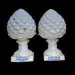 FÁBRICA DE DEVESAS JOSÉ P. VALENTE -  VILA NO DE GAIA  PORTO  PAR DE PINHAS ESCULTÓRICAS EM FAIANÇA ESMALTADAS COM EFEITO DE MARMORIZAÇÃO. MARCAS NA BASE FABRICA DEVEZAS J. P. VALENTE PORTO. PORTUGAL, SEUGUNDA METADE DO SEC. XIX. 43 CM DE ALTURANOTA:  em 1864, JOSÉ JOAQUIM TEIXEIRA LOPES viajou para Paris, onde se fixou durante dois anos. Na França, recebeu formação de François Jouffroy na École Impériale de Beaux-Arts, travando conhecimento com o formato telha Marselha. Foi lá que, desenvolveu as peças escultóricas A União faz a Força, que seria exposta no Ateneu Comercial do Porto, e na exposição trienal da Academia Portuense de Belas Artes, em 1866. Dois anos depois, regressou de um lugar onde só regressaria nas Exposições Universais de 1889-90, passando a centrar-se na produção cerâmica dentro de portas. Após trabalhar com Francisco Correia Breda, não se contentou com o trabalho de vidraria que fazia, e juntou-se a Almeida da Costa, tornando-se sócio na Cerâmica das Devesas. Para prolongar a sua vocação artística, fundou a sua própria escola de desenho e modelação, que, apesar do seu ensino decorrer durante a noite, viria a formar as bases para a constituição da Escola Industrial Passos Manuel. Entretanto, seria nomeado para Cavaleiro da Ordem de Cristo."Uma vez regressado a Portugal e rodeado da esposa e dos filhos, o artista abandona a intenção de regressar a França e toma a decisão de se meter ao trabalho imediatamente, começando por reproduzir em cerâmica ( certamente sob influência do desenvolvimento que esta indústria tinha atingido nas fábricas de Vale da Piedade e Miragaia) algumas figuras (como a sua estátua A União faz a força)  e vasos ornamentais modelados por ele, sem descurar também a produção de figurinhas de costumes .  Para o efeito, alugou nas Devesas (Gaia) um pequeno terreno onde construiu um forno e uma pequena oficina, para trabalhar a argila e moldar os gessos.  Na proximidade, alugou também uma pequena casa onde descansava, para não vir diariamente para a sua casa do Porto, na Rua de Miragaia, 146. A sua mulher, que estava grávida, mas não contava ter o filho tão cedo, não teve tempo para voltar ao Porto e acabou por dar à luz em Gaia. Foi por esta razão que nasceu António Teixeira Lopes, em 27 de Outubro de 1866, naquela modesta moradia, na R. Conselheiro Veloso da Cruz, 353, na qual a C. M. de Gaia mandou colocar uma placa em 1936. O destino fez com que Gaia contasse com mais um grande artista. Uma vez que a casa estava situada na proximidade do terreno onde tinha a oficina e aquela era relativamente próxima do local onde seria mais tarde erigido o edifício da Fábrica Cerâmica das Devezas, tal como existe atualmente, pode-se concluir que os imóveis utilizados por Teixeira Lopes foram mesmo o embrião desta fábrica.  Inicialmente, debateu-se com o problema da falta de compradores, fase difícil da sua vida. O seu primeiro grande cliente foi o engenheiro francês Charles Baumam, homem de grande distinção e reconhecida notável carreira profissional, muito estimado em Gaia, tendo-se tornado grandes amigos. De acordo com Ramiro Mourão, em 1866, o artista relaciona-se com Francisco Correia Breda, rapaz sério, que tinha alguns conhecimentos da indústria, em particular  sobre o fabrico de vidros, permitindo a Teixeira Lopes adquirir conhecimentos mais profundos sobre técnicas de acabamento de peças de cerâmica. Breda associa-se com ele muito passageiramente, porque pouco tempo depois Francisco Correia Breda regressa ao Brasil. (3)Deve colocar-se a hipótese da associação de Teixeira Lopes com Francisco Breda se ter iniciado logo após o seu regresso definitivo de Paris ( já poderiam conhecer-se anteriormente?) e a laboração cerâmica ter começado ainda em 1865, sendo marcadas peças com a firma Teixeira & C., como se verá abaixo. Justificar-se-ia, desta forma, a atribuição da data de 1865 como a da fundação de facto do núcleo inicial da  Fábrica de Cerâmica das Devesas,  que é assumida oficialmente no catálogo da Fábrica de 1910 e que vem assim corroborar a hipótese que se está a desenvolver. Aliás, que motivo ponderoso levaria a Fábrica de Cerâmica das Devesas a atribuir-se uma data de fundação diferente da real? De acordo com Ramiro Mourão, Teixeira Lopes não podendo, por falta de recursos, comprar a Breda por doze moedas a sua parte na sociedade, esta é adquirida por António Almeida da Costa (1832-1915), seu amigo desde o momento em que dirigiu o pedestal da estátua de D. Pedro V. Mourão é vago sobre o valor da quota de Breda, não informando qual o montante monetário total das doze moedas.Deve ser referido que Teixeira Lopes poderia ter continuado sozinho, dado que, apesar do que escreve Ramiro Mourão, não seria difícil a Teixeira Lopes adquirir a quota de Breda, uma vez que, tratando-se duma microempresa, o seu valor seria muito reduzido. Além disso, se os seus pais não teriam grande possibilidade de o ajudar, já o inverso se poderia dizer dos seus sogros, que eram abonados proprietários e certamente o apoiariam, pelo reconhecimento da capacidade e vontade que Teixeira Lopes demonstrava em desenvolver a sua actividade e, sobretudo, pela amizade que os unia, de tal forma que, devido à casa dos pais de José Joaquim ser pequena, era na habitação daqueles, casa rústica de apreciáveis dimensões, que o casal Teixeira Lopes/Rachel residia quando estavam na terra natal. Esta casa viria a ser herdada por Rachel e foi usada pelo casal e família até à última década do século XIX, época em que Teixeira Lopes mandou construir uma casa nova na sua quinta, embora continuassem a ocupar a anterior, devido ao volumoso agregado familiar. (4)Mas, o escultor ambicionava dar um salto qualitativo na sua actividade, transitando duma prática artesanal de pequena monta, para uma industrial de maior dimensão. Para tanto era-lhe necessário conseguir um sócio com apreciável capital próprio (ou com fácil acesso a crédito), disposto a aplicá-lo naquele negócio e de preferência com algum conhecimento da indústria, como tinha sido o caso de Breda. Teixeira Lopes já conhecia Almeida Costa há uns anos, devido às parcerias artístico-comerciais já existentes entre eles (pelo menos desde 1862), em diversas obras, muito antes da fundação da Fábrica de Cerâmica das Devesas, nomeadamente o fornecimento de modelos de estátuas por parte de Teixeira Lopes, para serem copiados em mármore/pedra na oficina de Almeida Costa.  As parcerias mais paradigmáticas foram as dos concursos para a realização dos monumentos a Passos Manuel, D. Pedro IV e D. Pedro V. O segundo concurso foi perdido, mas o primeiro e terceiro foram ganhos, tendo Teixeira Lopes, pela execução da estátua de D. Pedro V, obtido uma notoriedade imediata, o que aproveitou também a Almeida Costa e à sua oficina de mármores, que passou assim a poder dispor de um parceiro escultor destacado, que daria garantia de qualidade a qualquer obra futura que viesse a ser objecto de concurso. O que veio a suceder...Dito isto, e considerando o bom relacionamento, amizade mesmo, entre os dois parceiros, nada mais natural que Teixeira Lopes tenha convidado o segundo para substituir Breda. Por seu lado, Almeida Costa tinha visão e experiência suficientes para  compreender que esta era uma excelente oportunidade de diversificar a sua actividade de canteiro-marmorista, sendo a produção cerâmica uma área que lhe poderia aportar uma excelente mais valia e um bom complemento para a sua oficina de mármores.Almeida Costa reunia todas as condições: tinha dinheiro, adquirido através da sua oficina, sobretudo pela construção de capelas e jazigos funerários e elementos decorativos para os mesmos, tudo realizado em mármore, lioz ou granito, e de algumas empreitadas que a transcendiam, por requererem concurso de outras artes, de que são exemplo as referidas colaborações de Teixeira Lopes.A quota de Breda foi assim comprada por Almeida Costa, ficando cada sócio com metade do capital. Entretanto, Almeida Costa  já em 1864 se tinha instalado, em sociedade com João Bernardo de Almeida em terrenos a norte da actual Rua Conselheiro Veloso da Cruz, com a finalidade de produzir cal. Esta empresa dissolveu-se em 1866, tendo Almeida Costa adquirido a quota de Bernardo de Almeida, incluindo terrenos, e toma posse, por compra ou aprazamento, da maioria dos terrenos onde se viria a instalar a futura Fábrica Cerâmica das Devesas. (5)  Certo é que Teixeira Lopes foi o fundador do núcleo primitivo da Fábrica (com as modestas instalações já referidas), iniciada sob a firma  Teixeira & C.:O seu neto José Marcel afirma que Teixeira Lopes Foi o fundador da Fábrica de Cerâmica das Devesas, iniciada com a firma Teixeira & Cª. e só depois da entrada do sócio António de Almeida Costa tomou esse título Assim, embora os dois sócios tivessem paridade de quotas, a firma continua a ser Teixeira & C. e, em 1867, em estátuas assinadas Teix.ra  surge pela primeira vez um carimbo oval  com a marca Fábrica das Devezas. O nome de Costa só aparece na firma seguinte: Costa, Breda e Teixeira Lopes.Seu filho António confirma-o: meu pai fundou a Fábrica das Devesas onde trabalhou duramente mais de quarenta anos; mais tarde, aceitou-o (a Almeida Costa) como sócioJoaquim de Vasconcelos secunda estas afirmações, acrescentando informação adicional: a Fábrica de Cerâmica das Devesas tinha começado nas condições mais modestas em 1865 num barracão de madeira, com meia dúzia de oleiros. (8)Júlio Brandão refere sobre Teixeira Lopes: A Fábrica das Devesas, que criou e dirigiu artisticamente até há pouco, deve-lhe todo o seu esplendor e tôda a sua nomeada 