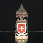 PORCELANA, um (1) tankard com ornamentação relevada e policromada sobre fundo azul cobalto, representando Brasão da Cidade Suíça de Schweiz, marcada em cavo na base 1000S Orig King, tampa em pewter, medindo 19 cm altura, sinais de uso, vide foto, ideal para coleção de bar.