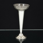 METAL PRATEADO, um (1) vaso floreiro no formato de corneto, base em degraus e com enchimento, borda vazada em geométricos, marcas parcialmente legíveis e não identificadas, medindo 22 cm altura, sinais de uso, vide foto.