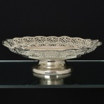 AÇO INOX, uma (1) fruteira de pé baixo, borda vazada em elementos vegetalistas, base ligeiramente cônica e lisa, marca WOLFF (tradição desde 1894), medindo 28,5 cm diâmetro e 8 cm altura, sinais de uso, vide foto.