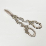 METAL PRATEADO, uma (1) tesoura de mourões, ornamentação relevada em parras, sem marca de manufatura aparente, medindo 16 cm comprimento, sinais de uso, vide foto.