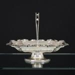 METAL PRATEADO, uma (1) antiga fruteira octogonal, ornamentação vazada em silhuetas vegetalistas e relevada em guirlandas de tulipas e perolados, fundo e moldura, cinzelada e burilada em elementos vegetalistas, base com saia perolada, alça dupla fixada por esferas, marca COOPER BROS (fundada em 1866, por Thomas Cooper e John William Cooper; em 1895 virou Cooper Brothers & Sons Ltd.; em 1983 foi vendida para a Frank Cobb & Co. Ltd.), medindo 30 x 22 x 24 cm de altura até a alça, sinais de uso, vide foto.