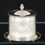 METAL PRATEADO, uma (1) caixa de chá oval, ornamentação em baixo relevo com pérgulas, volutas e elementos vegetalistas, borda da saia relevada em corda, tampa de abertura basculante com terminação em pinha, pés em bolachas, marca de origem Sheffield  England, medindo 19 x 15,5 x 16,5 cm, sinais de uso, vide foto.