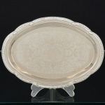 AÇO INOX, uma (1) bandeja oval, borda relevada em conchas e corda, fundo em baixo relevo representando volutas e elementos vegetalistas, medindo 24 x 17 cm, sinais de uso, vide foto.