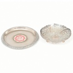 METAL PRATEADO, dois (2) itens: 1 mini fruteira vazada em elementos vegetalistas, base trípode em bolachas, marca MERIDIONAL, sinais de que já teve alça, medindo 8 cm diâmetro; 1 porta copo com propaganda central da N R K C, esquartelada dentro de uma estrela de oito pontas, borda relevada em corda, medindo 10 cm diâmetro, ambas com sinais de uso, vide foto.