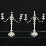 METAL PRATEADO, par (2) imponentes candelabros para três lumes cada, conversíveis para candelabro de dois lumes com ornamento de pira central ou para castiçal de um lume, ornamentação relevada em volutas, um deles ligeiramente inclinado, fundo com enchimento, patenteado na Inglaterra e Canadá, medindo 38,5 cm altura, sinais de uso, vide foto.