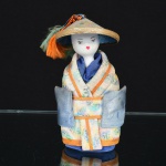 BRINQUEDO, uma (1) boneca oriental com cabeça em biscuit, vestes em tecido, papel, linha, etc., possui enchimento, medindo 14 cm altura, vide foto.