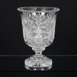CRISTAL, um (1) imponente vaso de pé alto, grosso, incolor e translúcido, lapidado em bico de jaca, estrelas e flores, fuste hexagonal, base em degraus com fundo estrelado, medindo 30 cm altura e 22 cm diâmetro, vide foto.