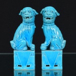 PORCELANA, par (2) esculturas representando casal de cães de fó  (sagrados animais fantásticos com aparência de leão que guardam os Templos Budistas, termo originário da China, pois fó significa Buda, geralmente representado como casal onde o macho brinca com uma bola que significa a terra e a fêmea protege a cria), na tonalidade azul turquesa, medindo 11,5 cm de altura.