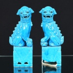 PORCELANA, par (2) esculturas representando casal de cães de fó  (sagrados animais fantásticos com aparência de leão que guardam os Templos Budistas, termo originário da China, pois fó significa Buda, geralmente representado como casal onde o macho brinca com uma bola que significa a terra e a fêmea protege a cria), na tonalidade azul turquesa, made in China, um deles com a base quebrada, medindo 25 cm de altura.