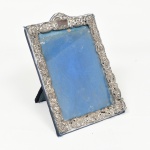 FOTOGRAFIA, um (1) porta-retratos retangular com apliques em prata, vazada em volutas e elementos vegetalistas, envidraçado, medindo 18,5 x 13 cm, sinais de uso, pequenos defeitos e perdas, vide foto.