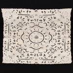 CAMA E MESA, uma (1) toalha quadrangular da Ilha da Madeira, tonalidade bege, bordado richelieu floral em linha castanho, medindo 82 x 82 cm, sinais de uso, vide foto.