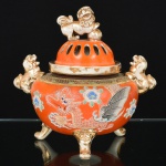 FAIANÇA JAPONESA, uma (1) urna com tampa, marcada em caracteres no verso Kutani, além da legenda de origem made in Japan, ornamentação relevada na técnica Moriage, representando Dragão Celestial, policromada sobre fundo na tonalidade coral, alças e pega da tampa representando Cães de Fó, generosos arremates a ouro já com sinais de desgastes, base trípode com pés relevados em máscaras, tampa vazada, medindo 23 cm altura, sinais de uso, vide foto.