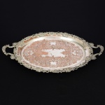METAL PRATEADO, uma (1) bandeja oval, fundo cinzelado e burilado em baixo relevo representando volutas e elementos vegetalistas, borda e alças reforçadas e relevadas em parras, medindo 58,5 x 3,5 cm até as alças, sinais de uso, vide foto.