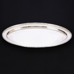 METAL PRATEADO, uma (1) travessa oval, ornamentação no padrão Império Napoleônico com frisos intercalados por X, medindo 59,5 x 33 cm, sem marca de manufatura aparente, sinais de uso, vide foto.