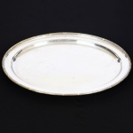 METAL PRATEADO, uma (1) travessa oval, ornamentação no padrão Império Napoleônico com frisos intercalados por X, medindo 54,5 x 40,5 cm, sem marca de manufatura aparente, sinais de uso, vide foto.