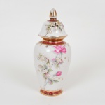 PORCELANA, um (1) antigo vaso com tampa, ornamentação floral policromada, faixas na tonalidade magenta, arremates a ouro já com sinais de desgastes, apliques em flores e folhas (faltando algumas), atelier de decoração não identificado, marca SÃO PAULO (fundada no ano de 1940 em São Caetano do Sul, SP, pelos irmãos Teixeira, técnicos oriundos da fabrica de Vista Alegre Portugal, que vieram ao Brasil para assessorar a implantação da fabrica Porcelana D. Pedro II, RJ, depois um dos irmãos foi convidado a trabalhar em São Caetano do Sul no mesmo ramo, em 1939 os irmãos uniram-se novamente e fundaram em 1940 a Teixeira Barreto & Cia, posteriormente Virgílio Teixeira & Irmão, ambas usavam o nome fantasia Porcelana São Paulo, em 1981 tornou-se Porcelana Teixeira Ltda, ainda em atividade), medindo 27 cm altura, vide foto.