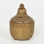 METAL, um (1) incensório com tampa encimada pela figura de BUDDHA (popularmente conhecido como SIDDHARTHA GAUTAMA, foi um príncipe de uma região no sul do atual Nepal que, tendo renunciado ao trono, se dedicou à busca da erradicação das causas do sofrimento humano e de todos os seres, e desta forma encontrou um caminho até ao despertar ou iluminação), na posição de lótus, lateral arrematada por barrado grego, marca de origem made in Japan, tonalidade bronze, medindo 7 cm altura, vide foto.
