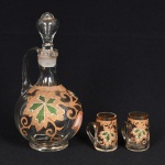 VIDRO VENEZIANO, conjunto com três (3) itens: 1 licoreira com tampa, incolor e translúcida, esmaltação floral policromada com generosos arremates a ouro, medindo 19,5 cm altura; 2 canequinhas na mesma padronização, medindo 5 cm altura, sinais de uso, vide foto.